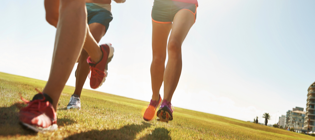 A group of runners take an energized jog through the park on a sunny day.