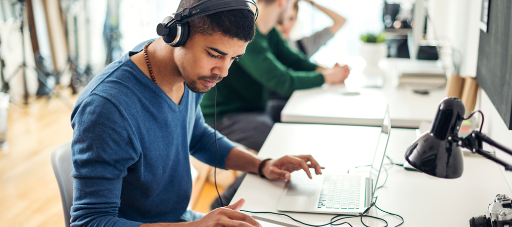 Young man employs noise-cancelling headphones to stay focused in an open office environment.