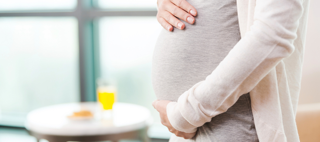 Expectant mother rests her hands on her baby bump.