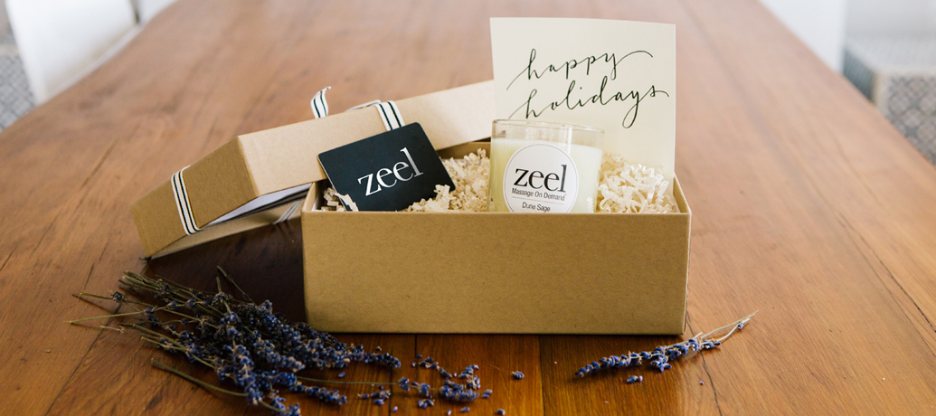 An opened gift box reveals a Zeel gift card, a Dune Sage candle, and a card hand lettered with "Happy Holidays".