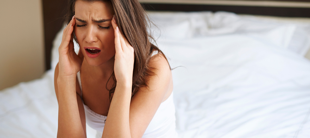 Girl applies pressure to her temples as she winces in pain from a hangover.