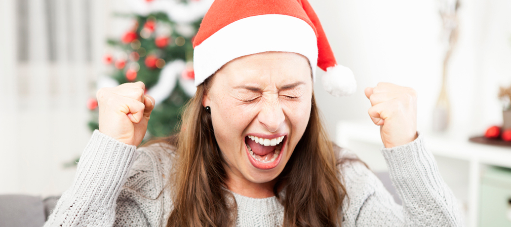 Girl in Santa hat screams and shakes her fists in the air with exasperation from holiday stress.