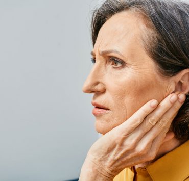 An elderly woman looking in the distacne and holding her ear in pain due to her tinnitus.