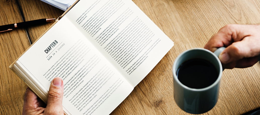 A person reading a book with a cup of coffee at home.