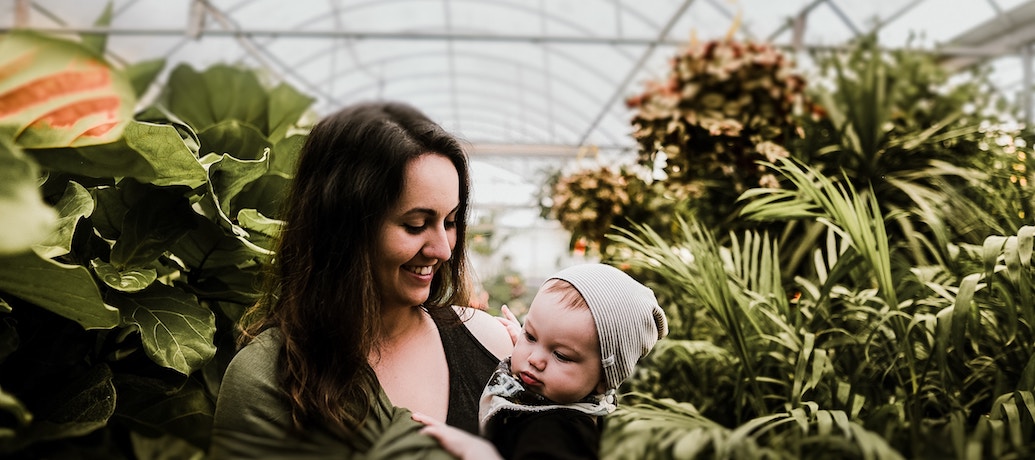 A woman smiling while holding her baby as she navigates through her postpartum recovery.