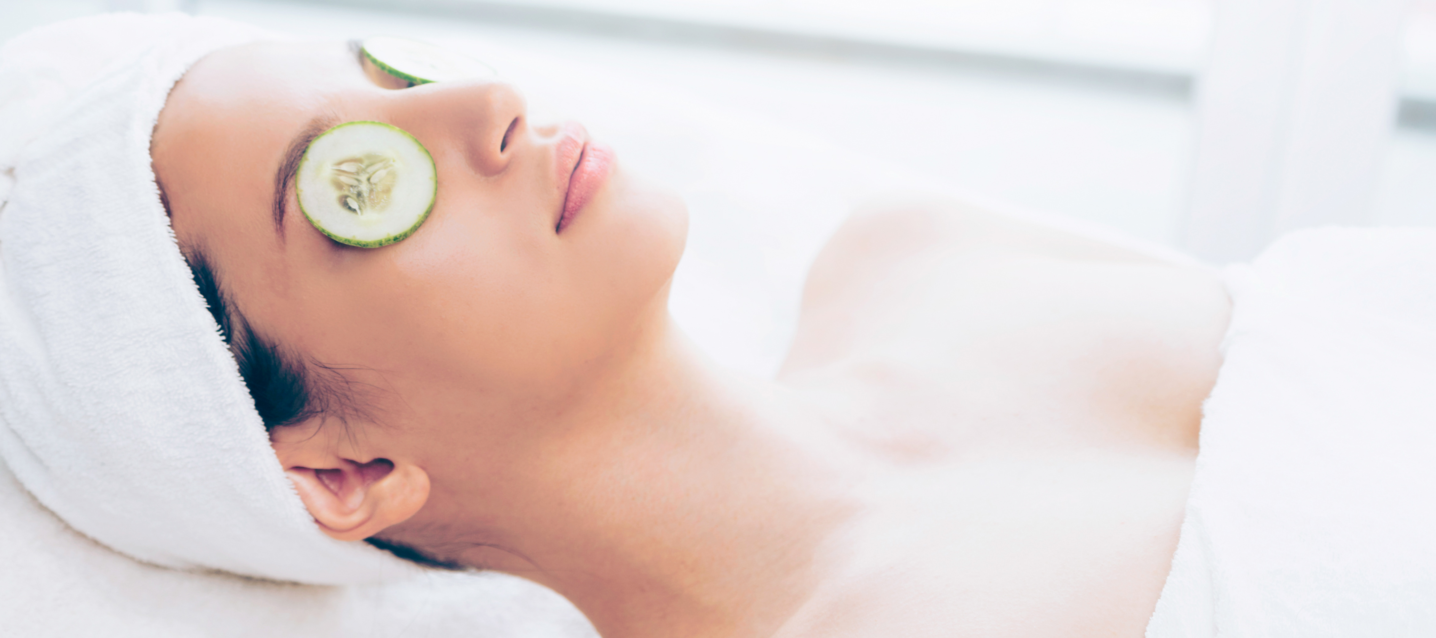 A woman relaxing with cucumbers over her eyes as she is about to receive a facial massage.