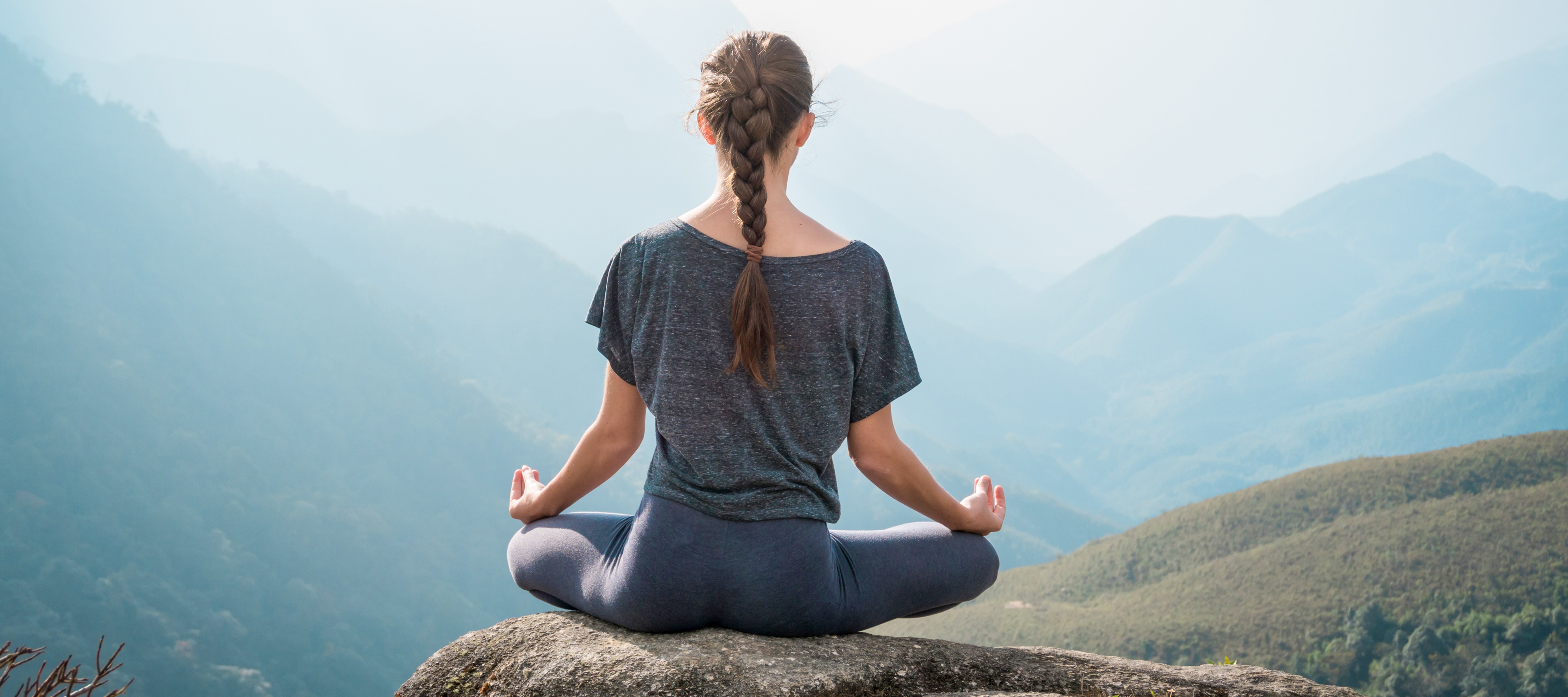 A woman sitting on the edge of a cliff to meditate as she practices mindfulness.