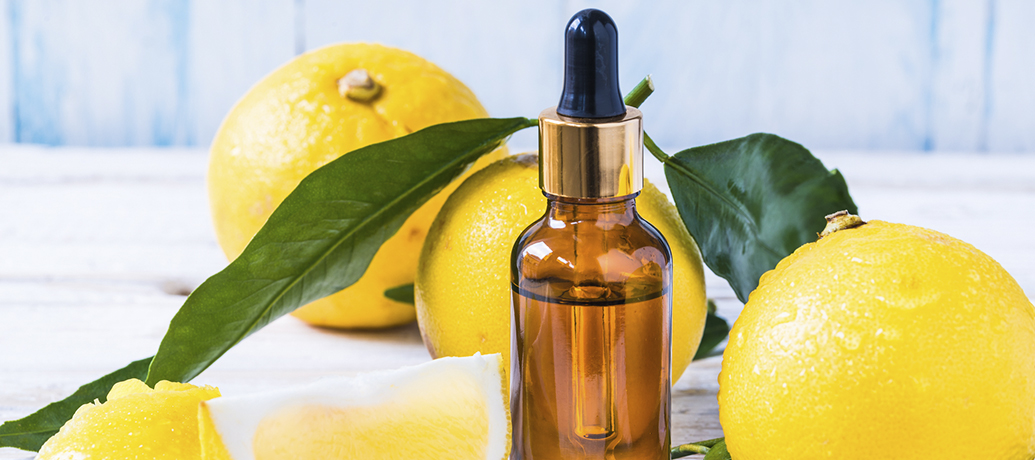 An oil used as a massage product sitting next to some lemons on a table.