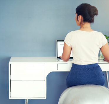 A woman sitting on an exercise ball at her WFH workspace.