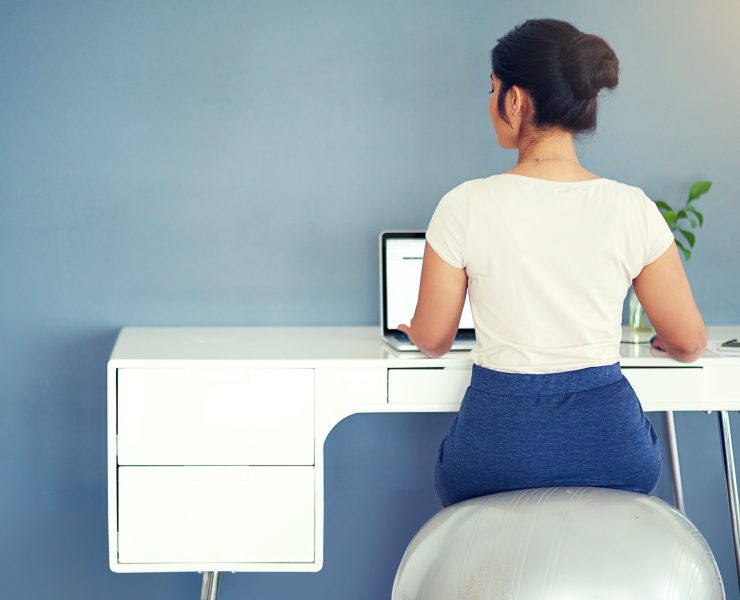 A woman sitting on an exercise ball at her WFH workspace.