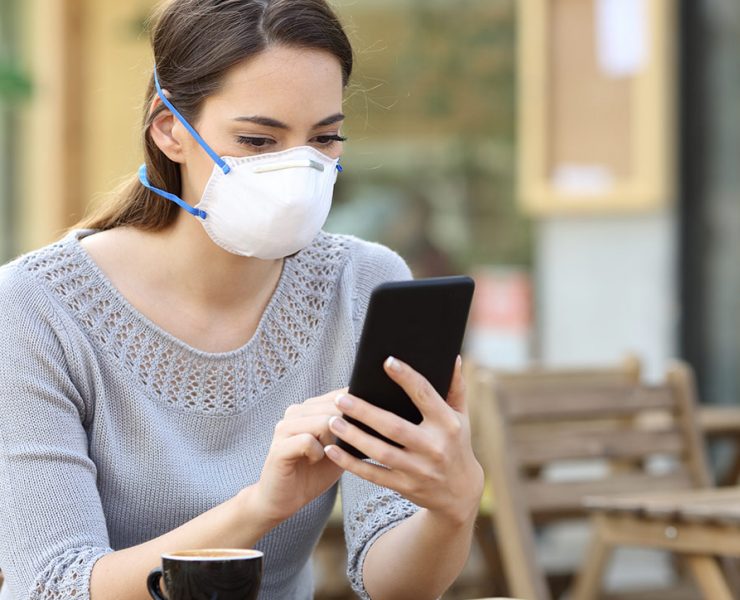 A woman sitting outside on her phone while wearing her mask as PPE during the pandemic.