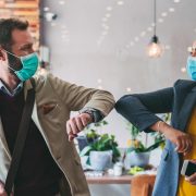 Two people bumping elbows while wearing PPE to safely greet each other during the pandemic.