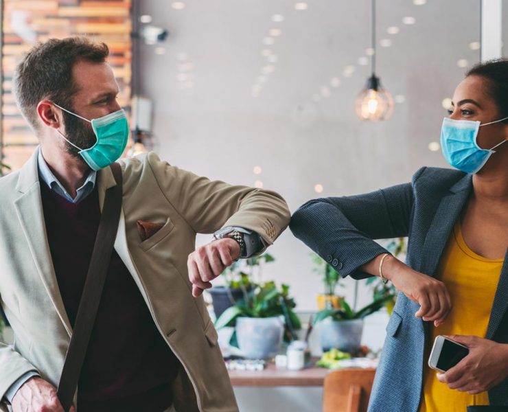 Two people bumping elbows while wearing PPE to safely greet each other during the pandemic.