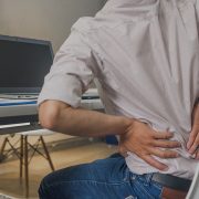 A man holing his lower back in pain as he sits at his desk since he forgot to to his upper body stretch for the day.