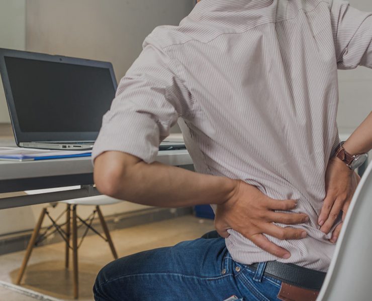 A man holing his lower back in pain as he sits at his desk since he forgot to to his upper body stretch for the day.