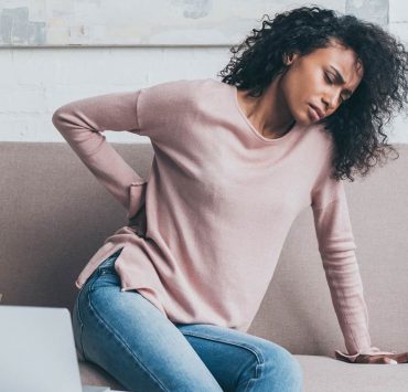 A tense woman holding her back in pain due to her poor posture.