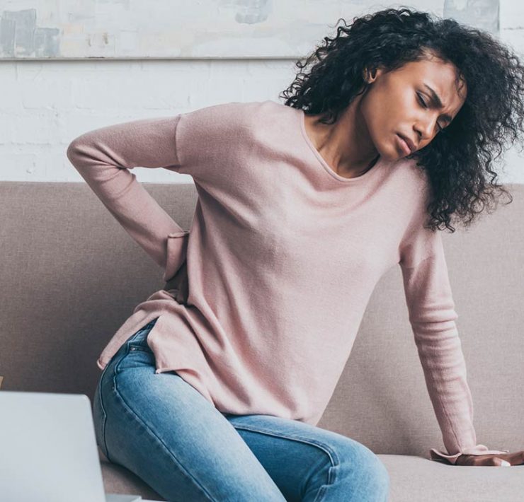 A tense woman holding her back in pain due to her poor posture.