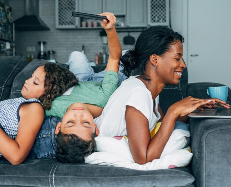 A mother sitting down at her computer while her children play behind her.