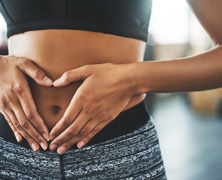 A woman facing digestive issues makes a heart shape over her stomach.