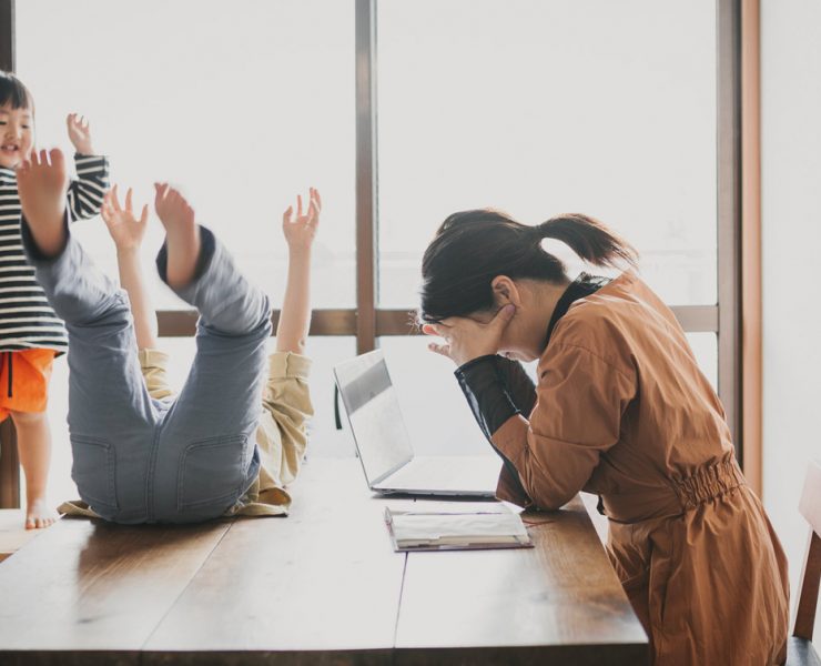 Kids playing on a woman's desk while she's working and thinking about incorporating a workout into her routine.