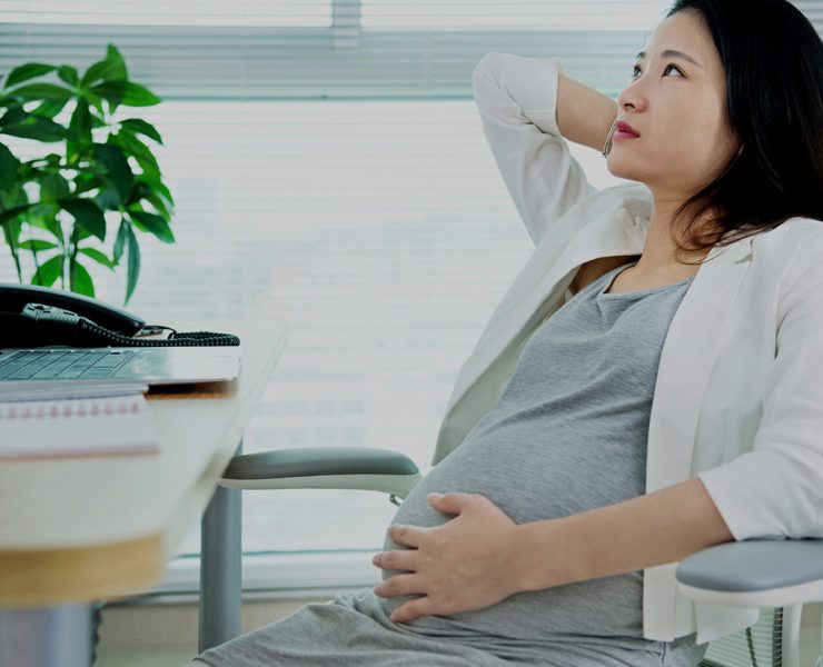A pregnant woman sitting in a chair looking uncomfortable due to her MSK pain.