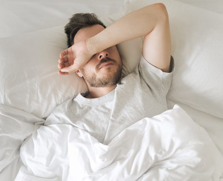 A man laying restless in his bed as he waits for his melatonin to kick in.