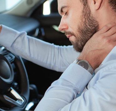 A man holding his neck in pain from lack of stretching while driving.