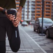 A person standing outside and stretching their leg to imp their circulation while exercising.