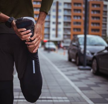 A person standing outside and stretching their leg to imp their circulation while exercising.