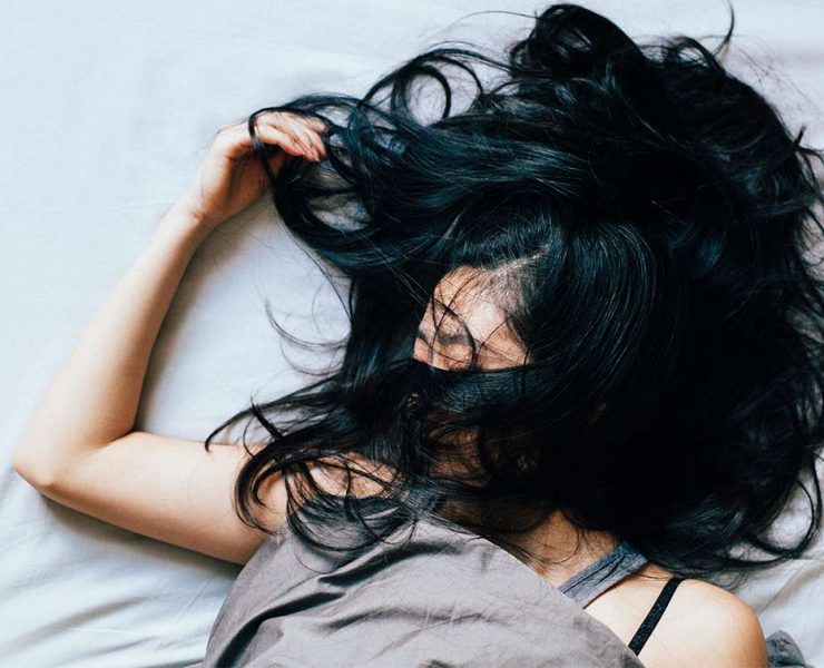 A woman laying in bed with her hair covering her face from twising and turening through the night due to her insomnia.