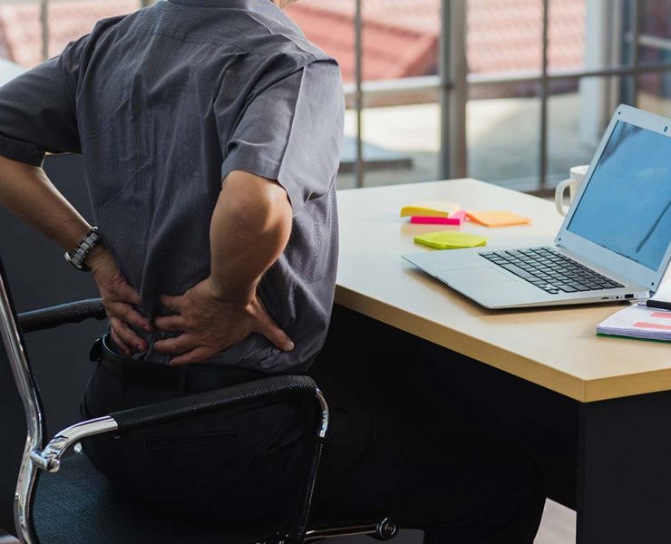 A man standing and holding his lower back to fix the discomfort he's feeling from his poor posture.