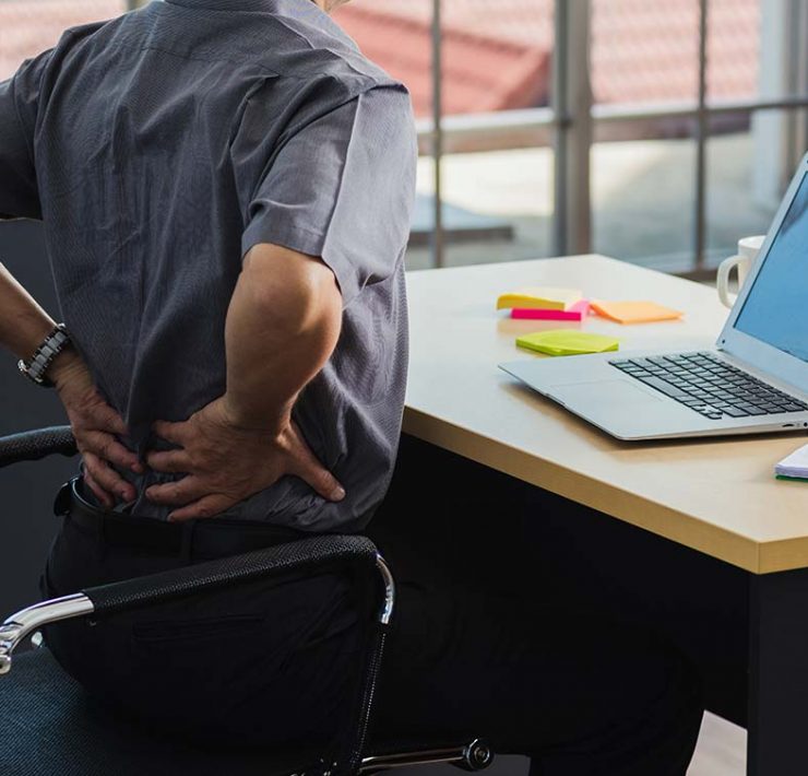 A man standing and holding his lower back to fix the discomfort he's feeling from his poor posture.