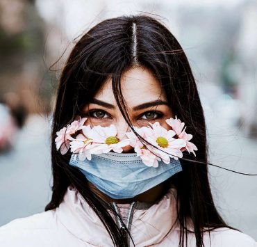 A woman practicing wellness by meditation in nature with flowers beneath her mask.