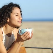 A woman having a drink on the beach as she prasctices mindfulness and takes the time to check in with herself.