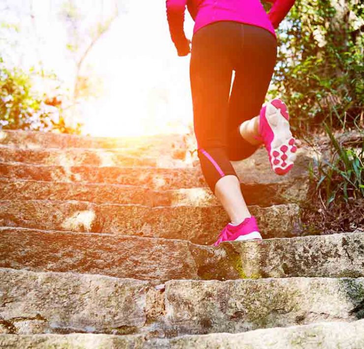 A woman exercising outside by running up a flight of stairs.