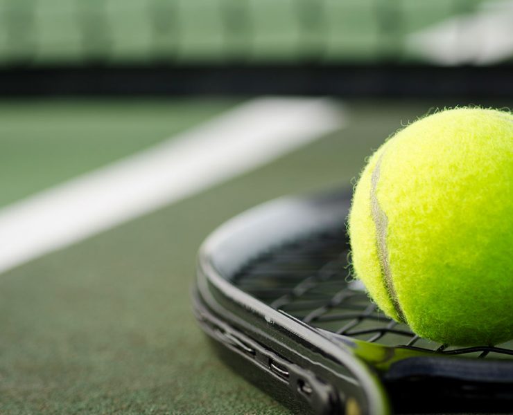 A tennis racket and ball are sitting on the court after the owner sat them down to stretch.