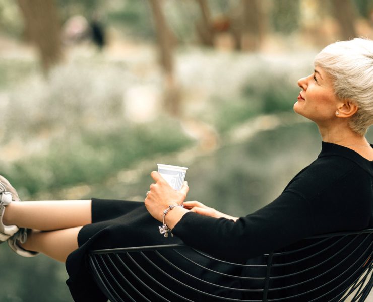 An older woman sitting outside relaxing with a drink in her hand as she follows thew blue zone living theory.