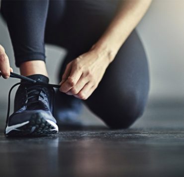 A woman tying her shoe to ensure that they're properly fitted to preserve her foot health.