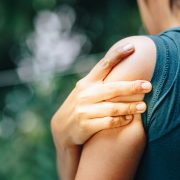 A woman holding her shoulder as she experiences pain from a pinched nerve.