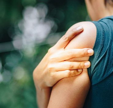 A woman holding her shoulder as she experiences pain from a pinched nerve.