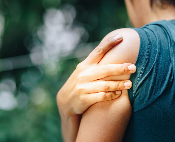 A woman holding her shoulder as she experiences pain from a pinched nerve.