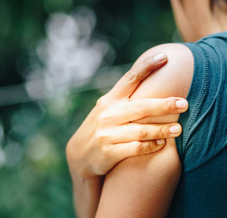 A woman holding her shoulder as she experiences pain from a pinched nerve.