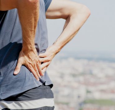 A man standing on the beach holding his lower back to ease he pain he is experiencing.