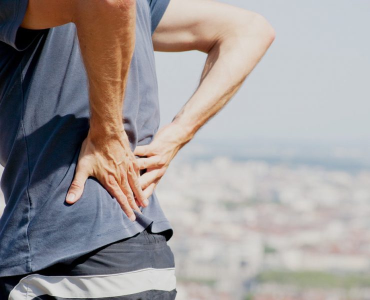 A man standing on the beach holding his lower back to ease he pain he is experiencing.
