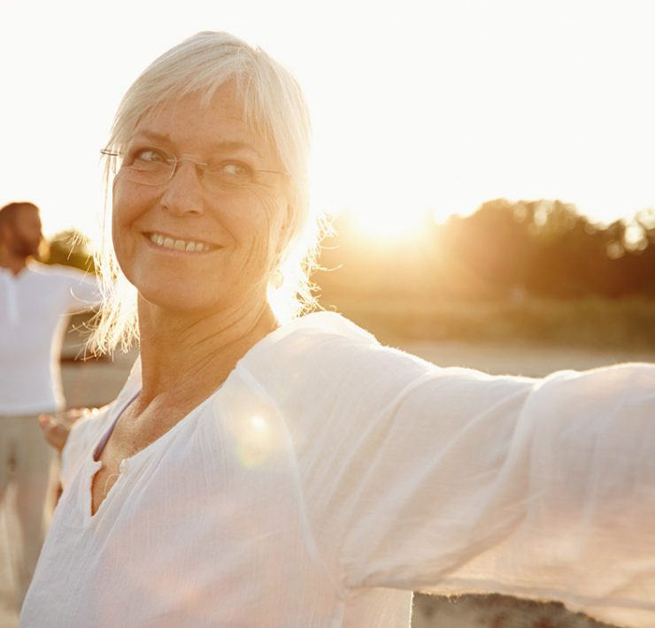 An elderly couple smiling and dancing outside after their massage therapy session for aging individuals.