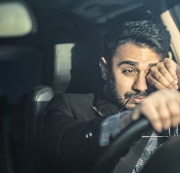 A man suffering from sleep deprivation as he rubs his eyes to stay awake while driving.
