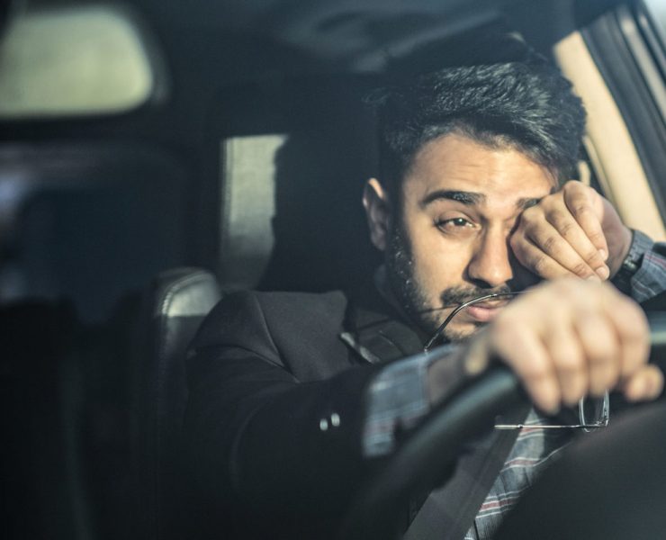 A man suffering from sleep deprivation as he rubs his eyes to stay awake while driving.